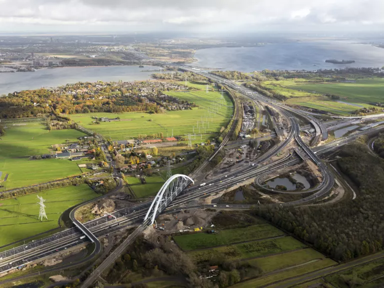 Snelwegknooppunt met een boogbrug in het polderlandschap, vanuit de lucht