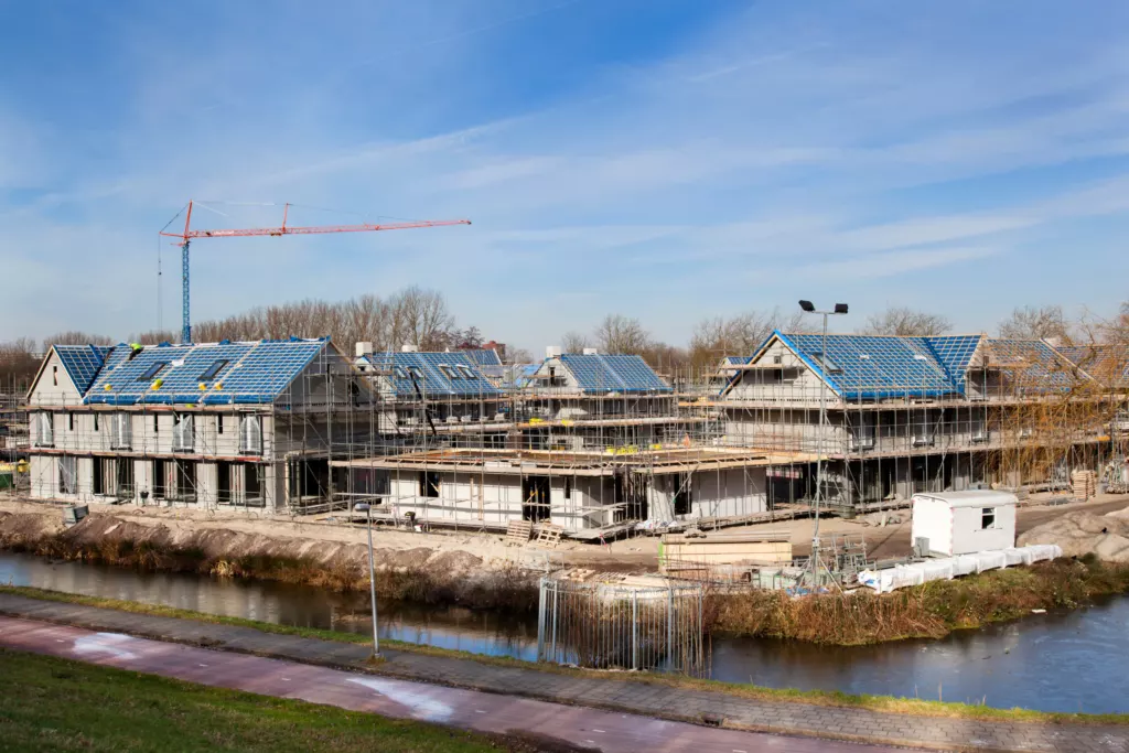 Nieuwbouwwoningen in aanbouw met zonnepanelen en een bouwkraan aan het water