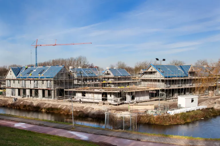 Nieuwbouwwoningen in aanbouw met zonnepanelen en een bouwkraan aan het water