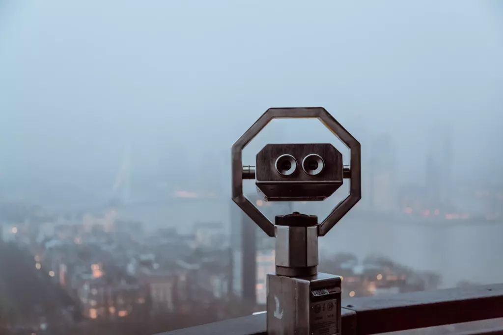 Verrekijker op een uitkijkpunt boven een stad in de ochtendnevel