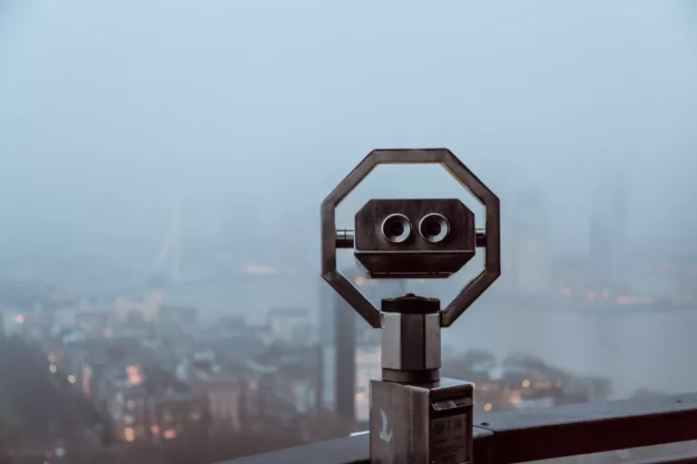Verrekijker op een uitkijkpunt boven een stad in de ochtendnevel