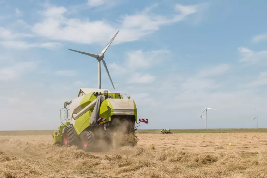Windturbine boven een akker waar een balenpers stro oppakt